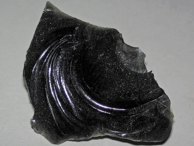 Obsidienne (SiO₂ (verre volcanique)) : minéral de la famille « silicates (tectosilicates) », système amorphe, dureté 5 à 5,5 (Mohs), couleurs : noir, brun, gris, irisé